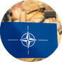 Vilnius, Lithuania - March 29 2022: Flag and symbol of NATO alliance, force integration unit with out of focus group of soldiers and military vehicles on background